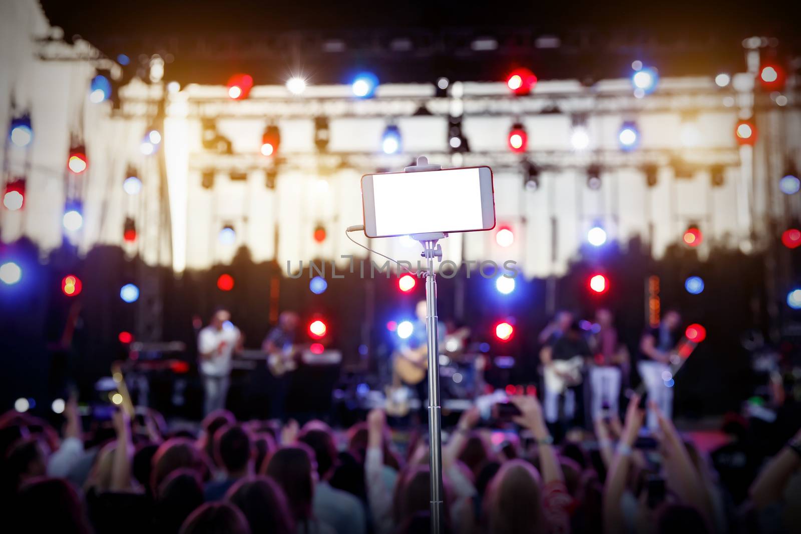 Using smartphone on a selfie stick at a music show. Empty blank white screen for your image.