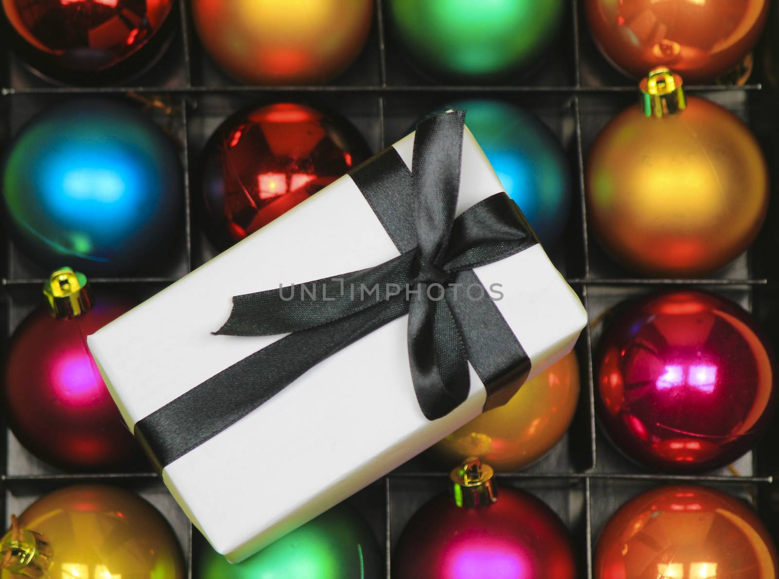 Gift wrapped with white paper and black bow on multicolor Christmas balls