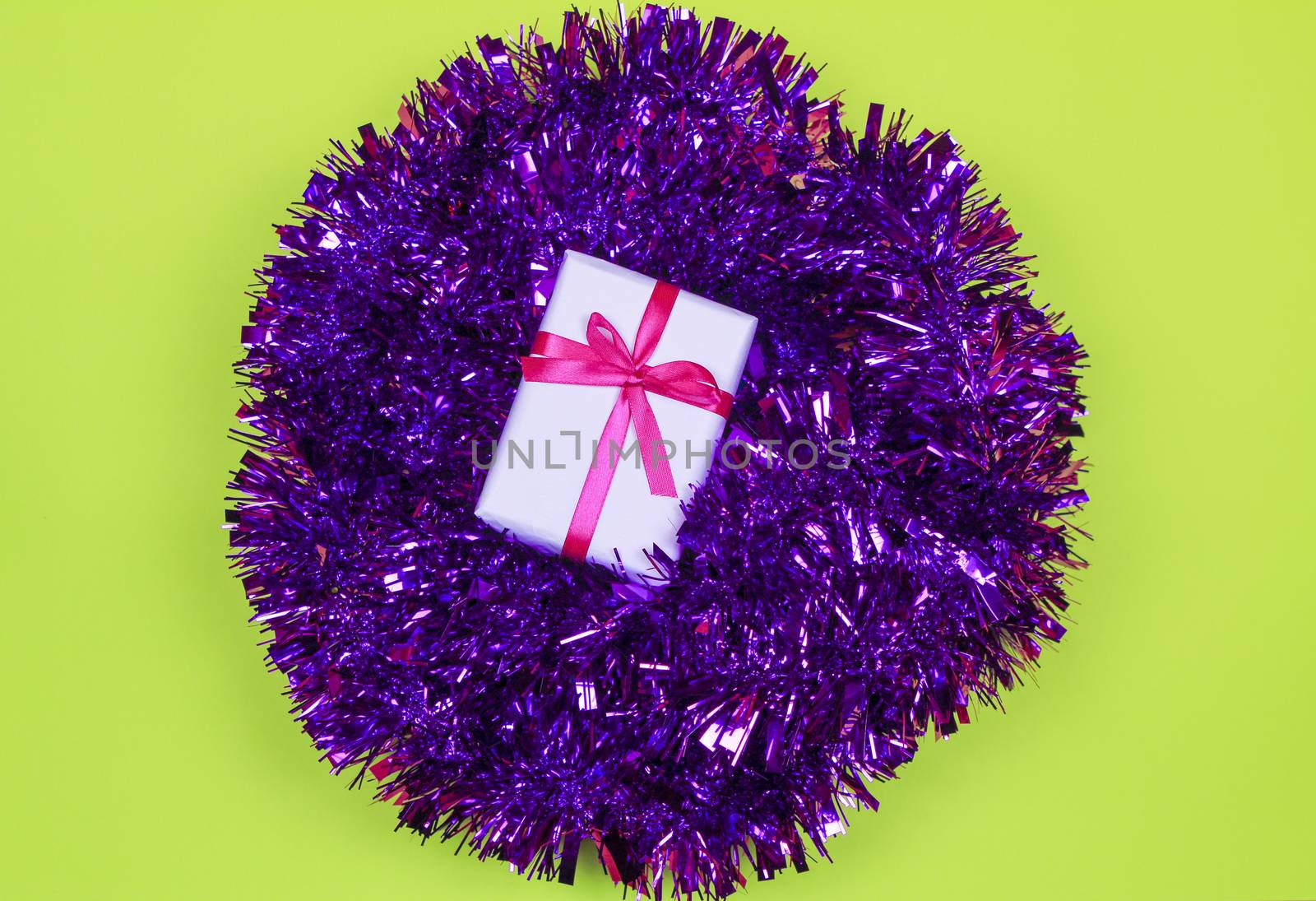 Gift wrapped with white paper and pink bow on purple tinsel on green background