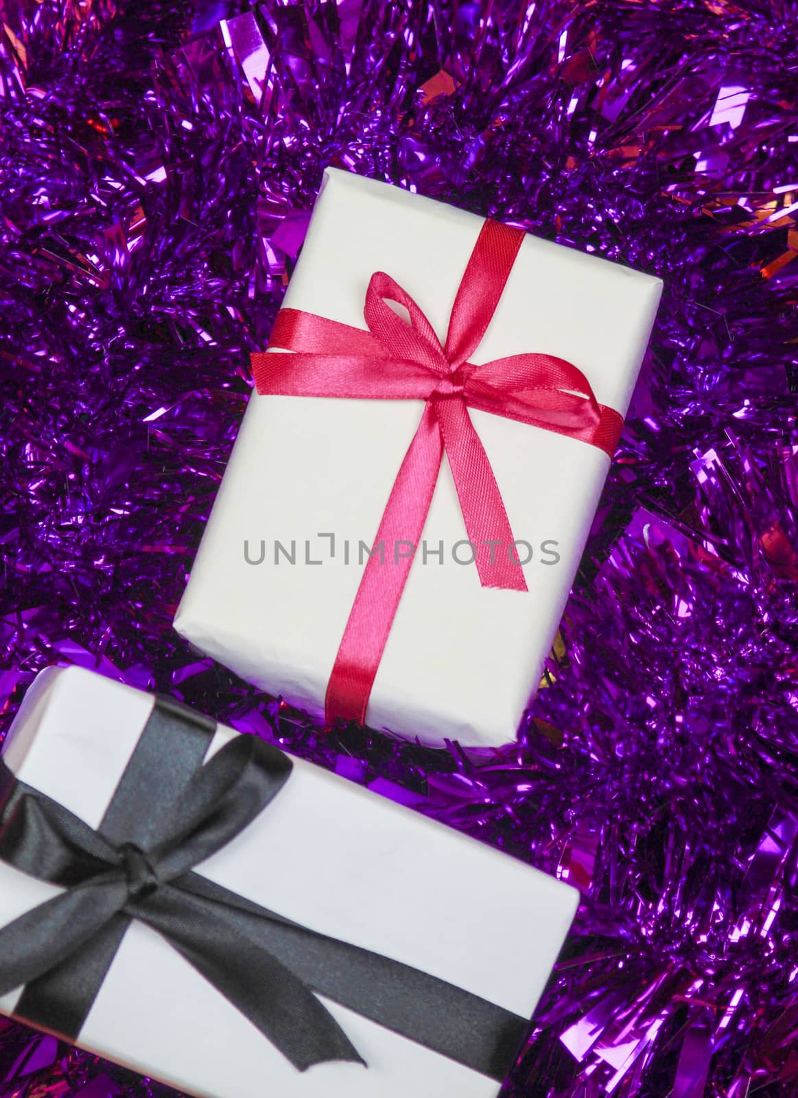 Gifts wrapped with white paper and pink and black bows on purple tinsel
