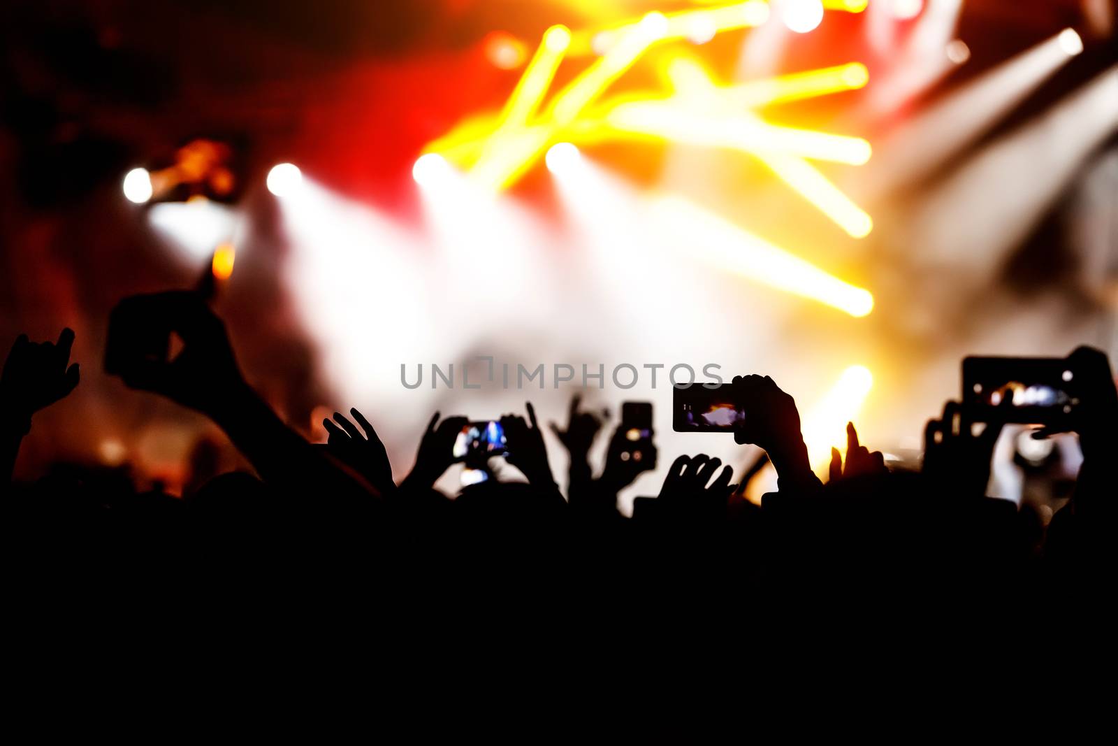 Silhouette of hands using camera phone to take pictures and videos at live concert.