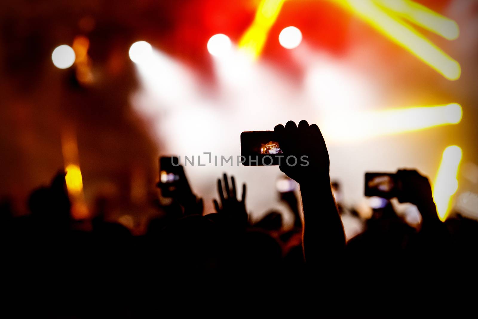 Silhouette of hands using camera phone to take pictures and videos at live concert.