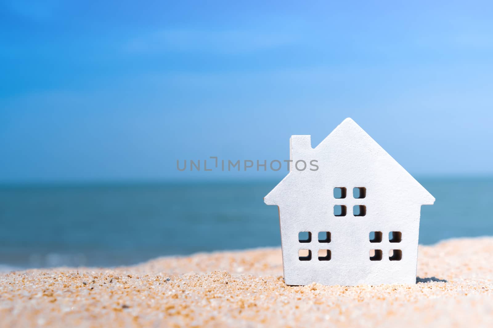 Closed up tiny home models on sand with sunlight and beach background.