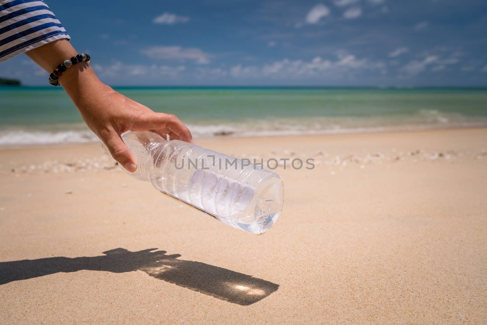 Hand pick up empty water bottle or trash at beautiful beach. Environment Global warming issue.  