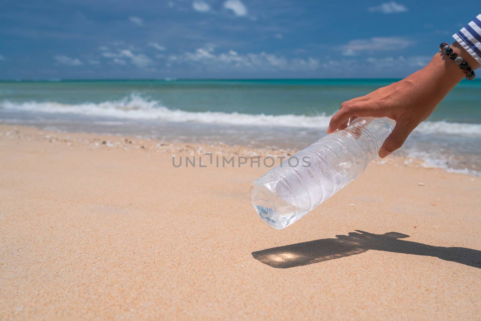 Hand pick up empty water bottle or trash at beautiful beach. Environment Global warming issue.  