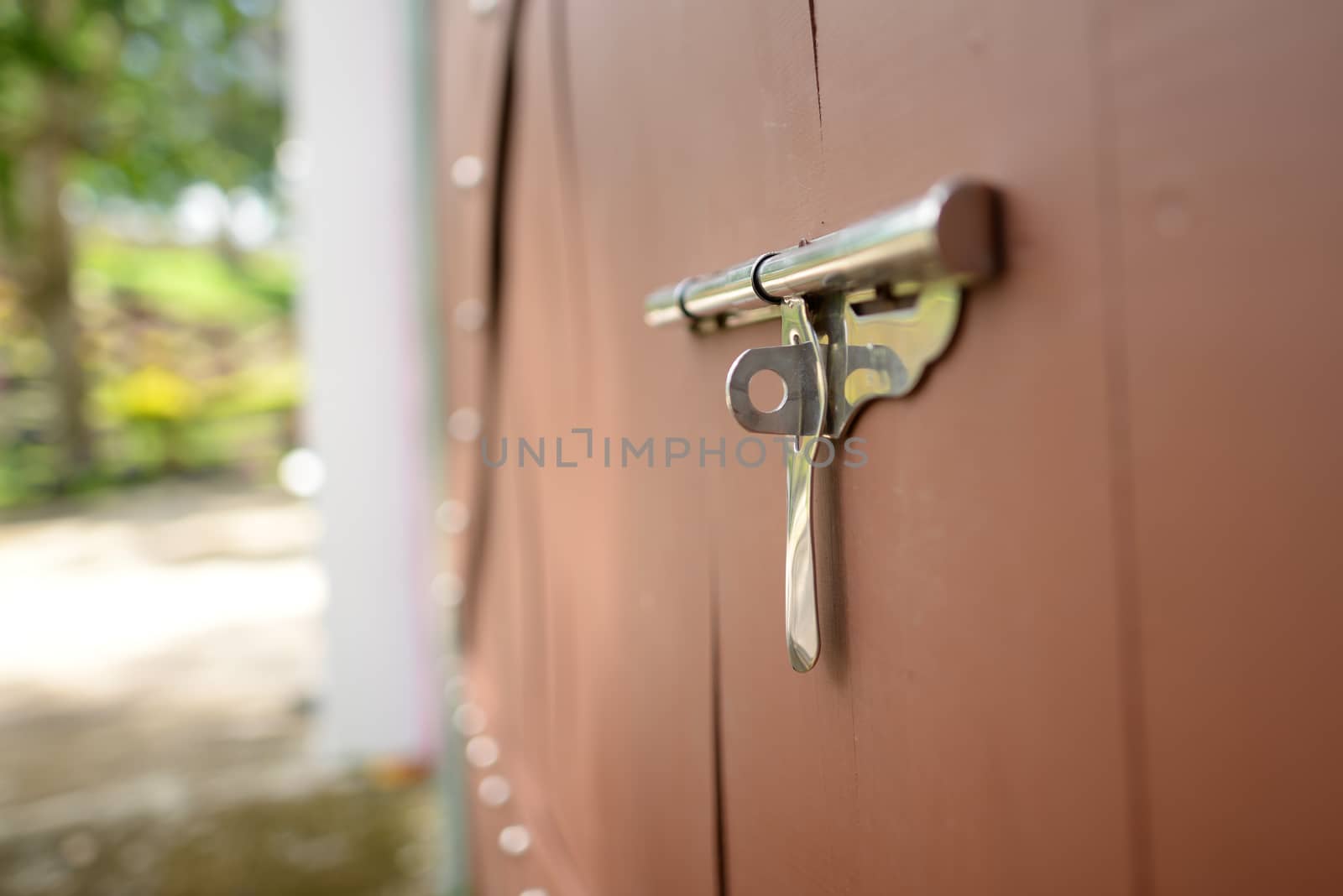 Stainless steel latch on a blurry brown wood floor. Focus on the key ring hole