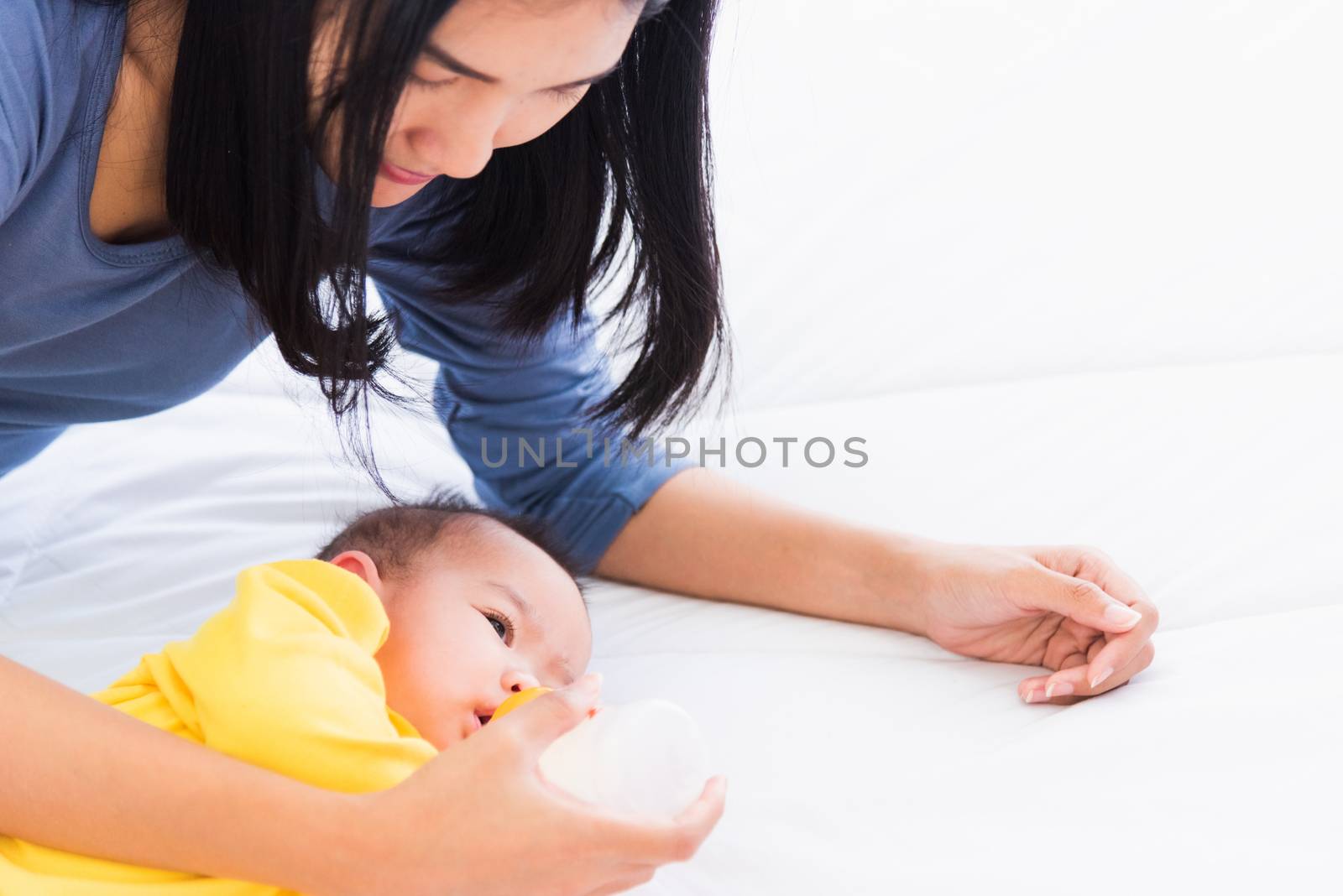 Portrait of beautiful young Asian mother holding and feeding infant newborn baby from milk bottle in a white bed, The child drinking milk from mom, Healthcare and medical