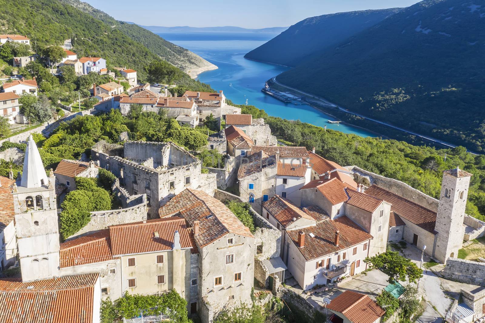 an aerial view of Plomin and Parish Church of the Blessed Virgin Mary with a bell tower, in background Plomin channel, Istria, Croatia