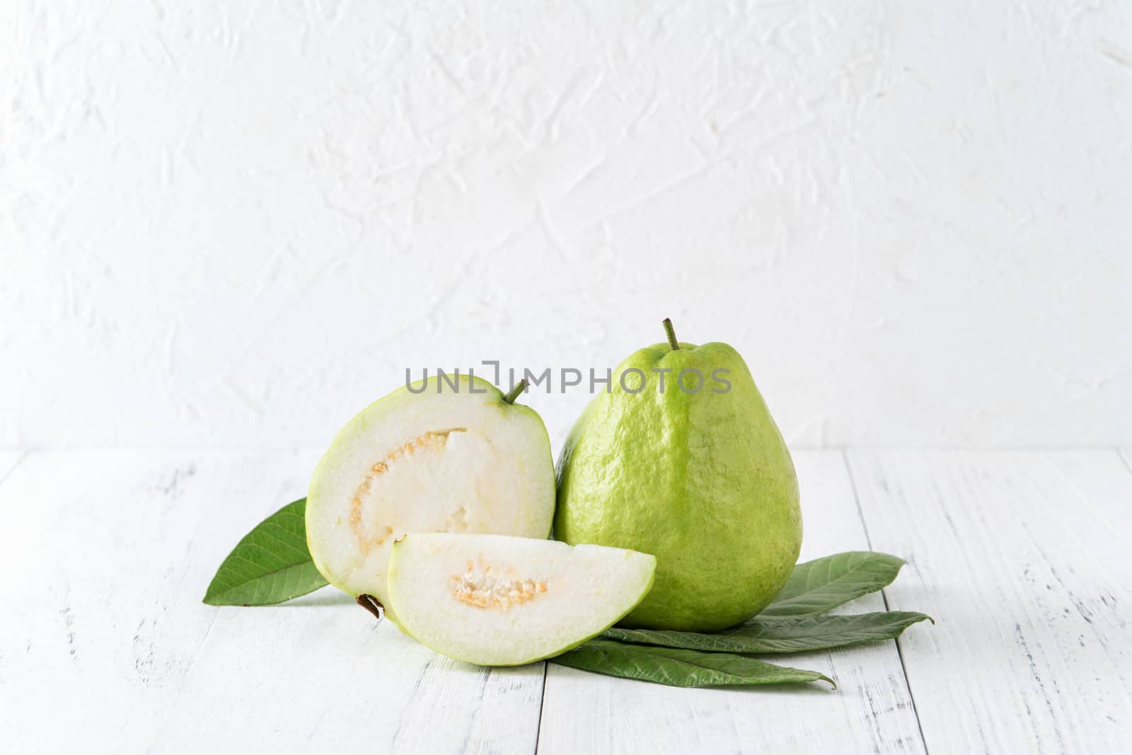 Delicious beautiful guava set with fresh leaves isolated on bright white wooden table background, close up.