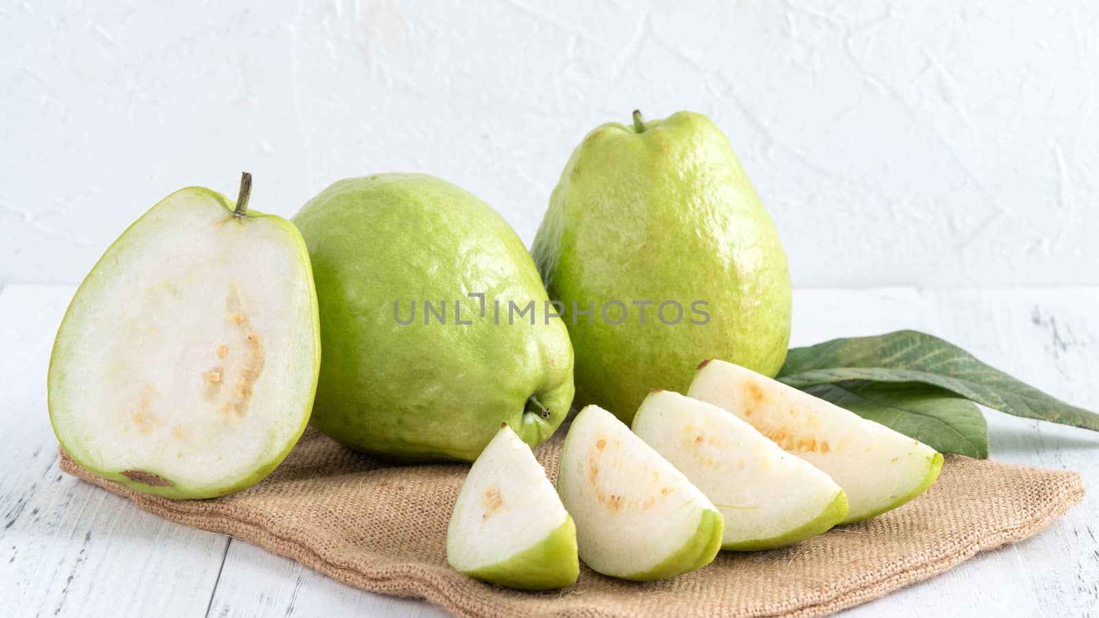 Delicious beautiful guava set with fresh leaves isolated on bright white wooden table background, close up.