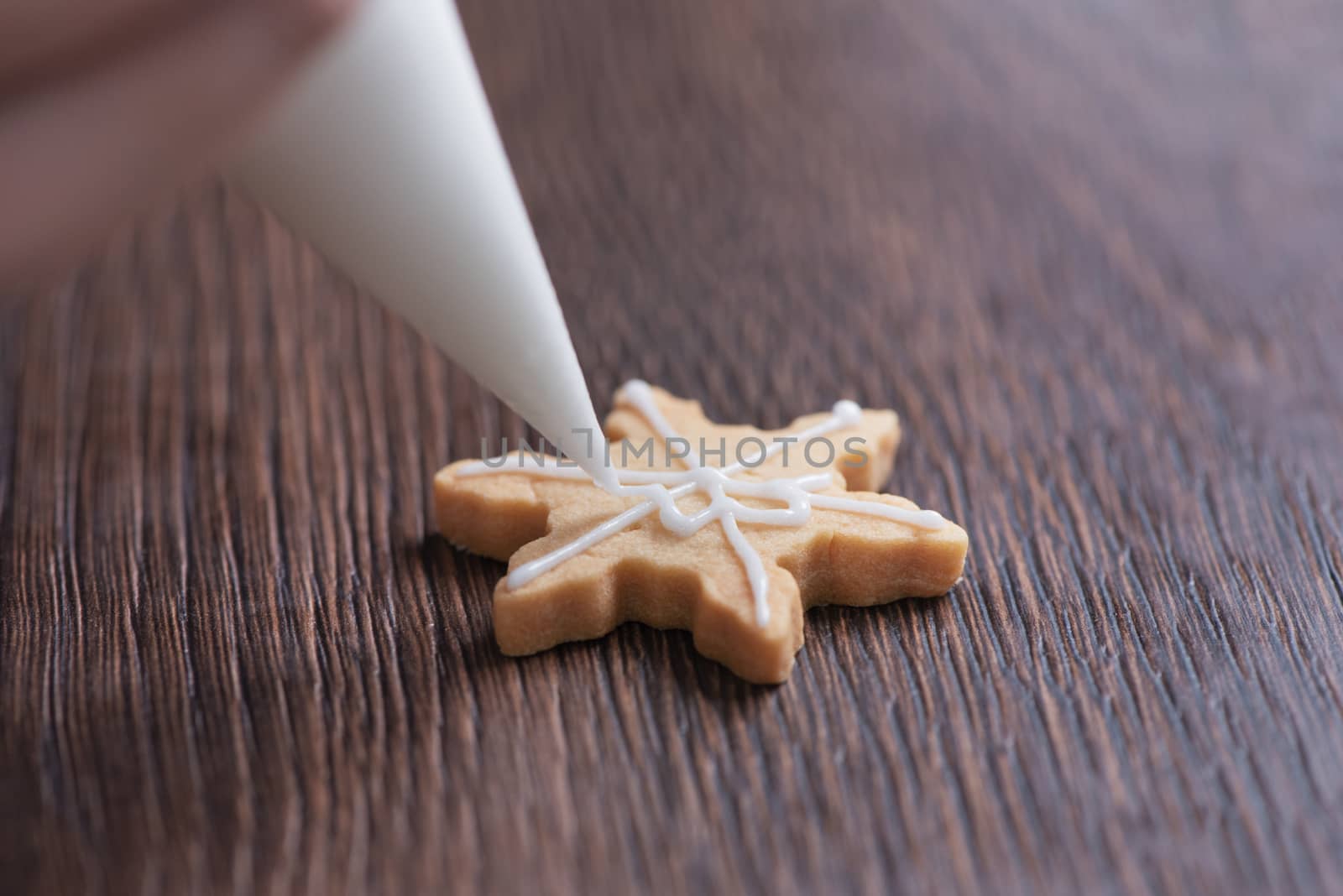Close up of drawing gingerbread Christmas snowflake sugar cookie on wooden table background with white icing, concept of holiday celebration.