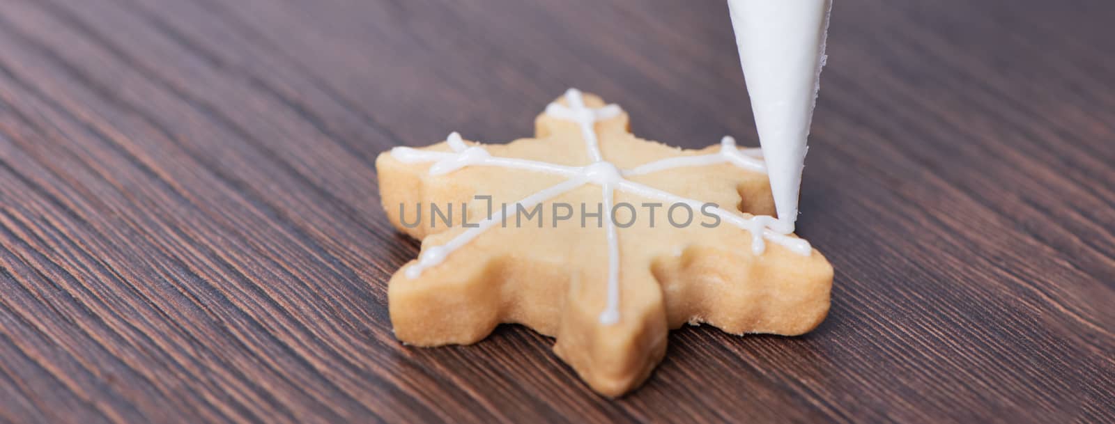 Close up of drawing gingerbread Christmas snowflake sugar cookie on wooden table background with white icing, concept of holiday celebration.