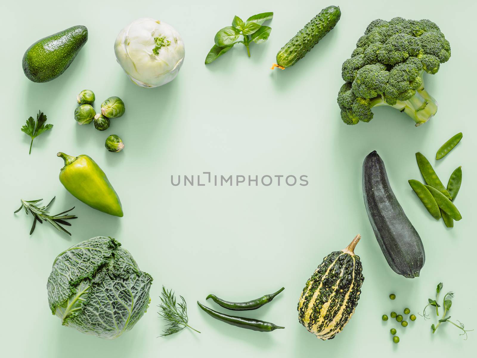 Green monochrome flat lay composition with vegetables, copy space in center. Vegetables - green peas, zucchini, avocado, bean-pod, pumpkin, broccoli, brussels sprouts, rosemary, microgreens. Top view