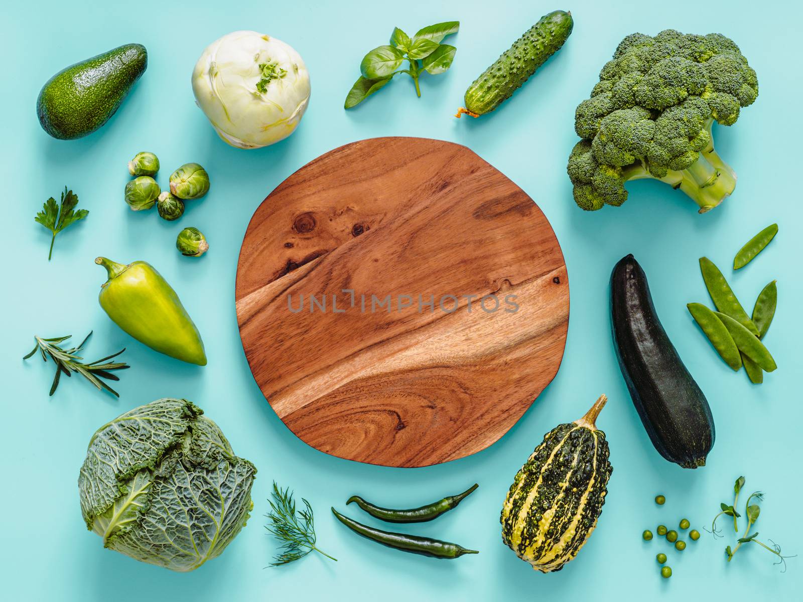 Flat lay with green vegetables on blue background, with circle wooden tray in center. Green peas, zucchini, avocado, bean-pod, pumpkin, broccoli, brussels sprouts, rosemary, microgreens. Copy space
