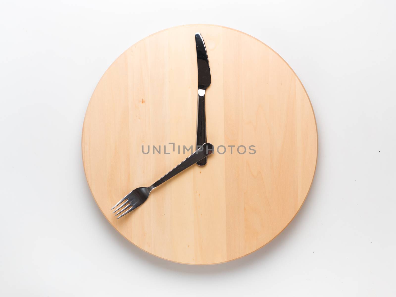 Intermittent fasting and skip breakfast concept - empty wooden round tray or trencher with cutlery as clock hands on white background. Eight hour feeding window concept or breakfast time concept.