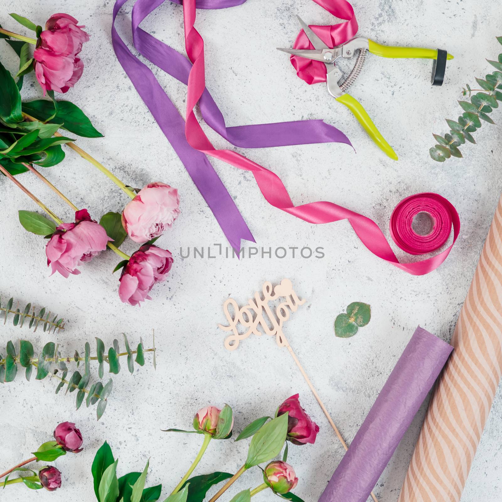 Floristic flat lay. Flowers, wrapping paper, ribbons and Love you wooden sign on gray tabletop. Copy space. Square format. Can use for social media posting