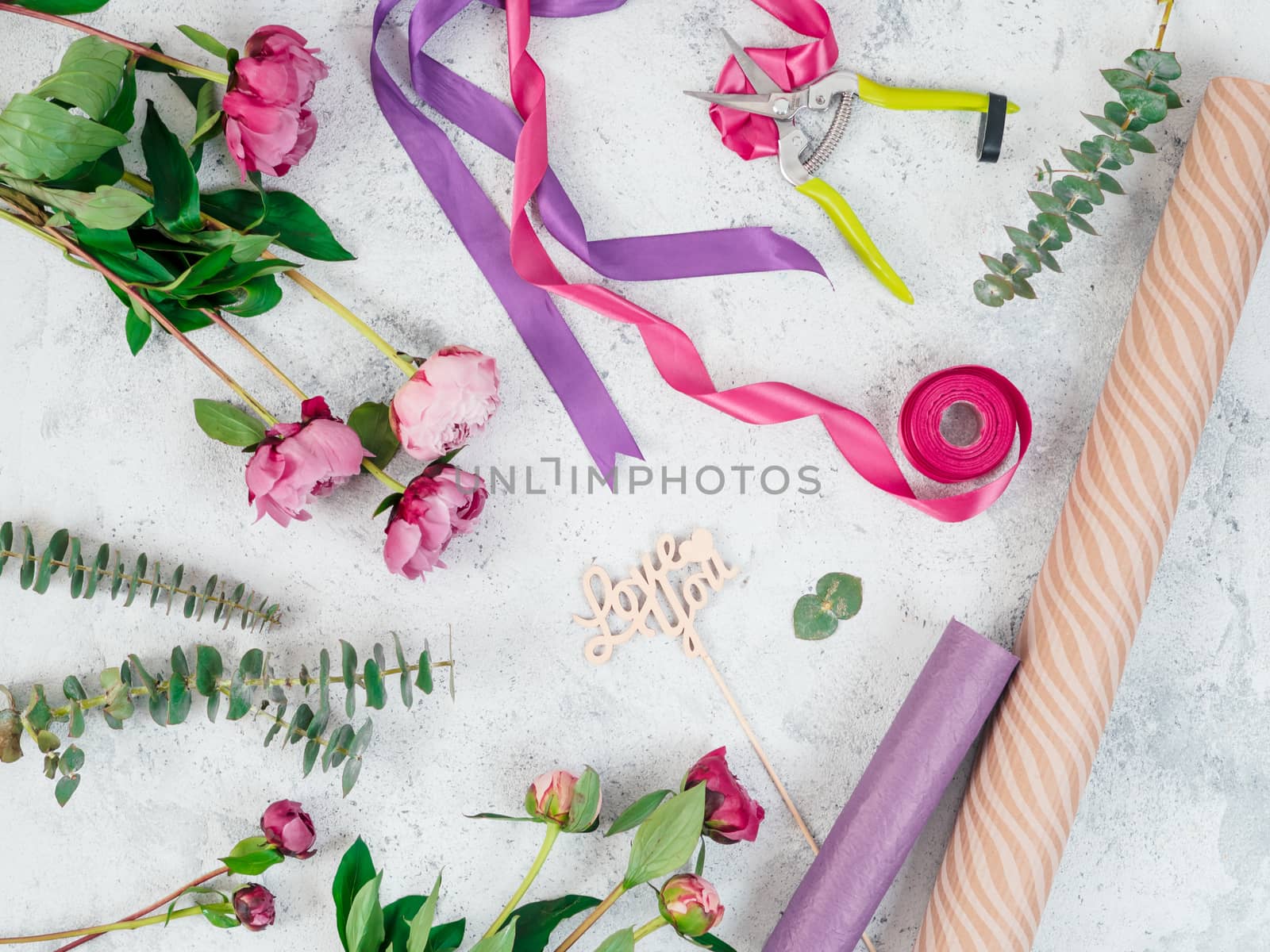 Floristic flat lay. Flowers, wrapping paper, ribbons and Love you wooden sign on gray tabletop. Roses, eucalyptus, Copy space. Can use for social media posting