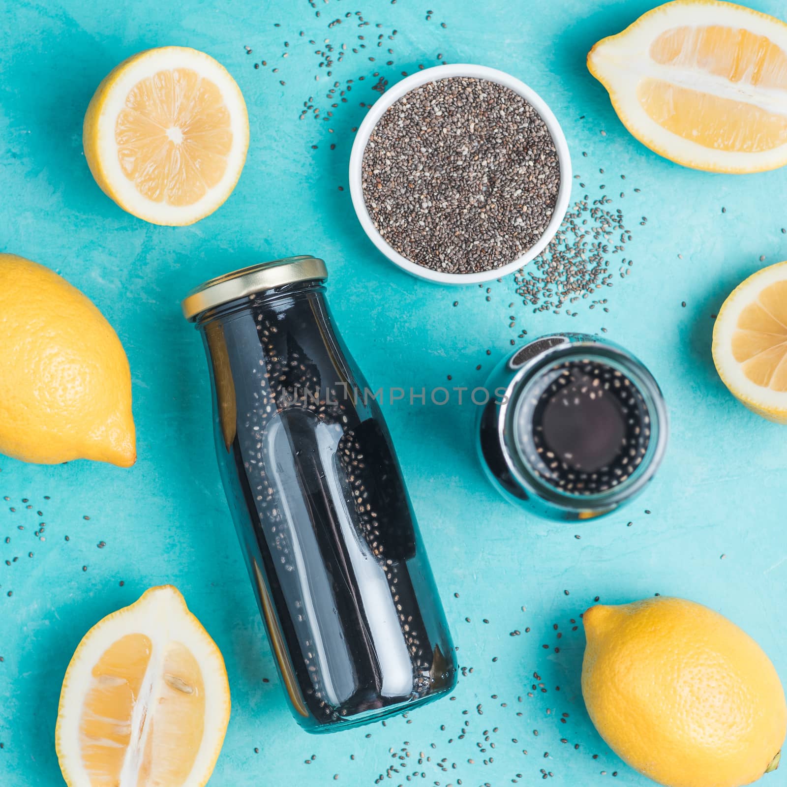 Detox activated charcoal black chia water or lemonade with lemon on bright blue background. Two bottle with black chia infused water. Detox drink idea and recipe. Vegan food and drink. Top view.