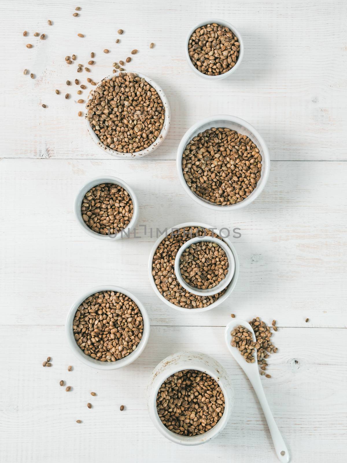 Hemp seeds in small white bowls and spoon on white wooden table. Set of small bowls with raw organic unrefined hemp seed. Superfood and vegan concept. Top view or flat lay.Copy space for text.Vertical