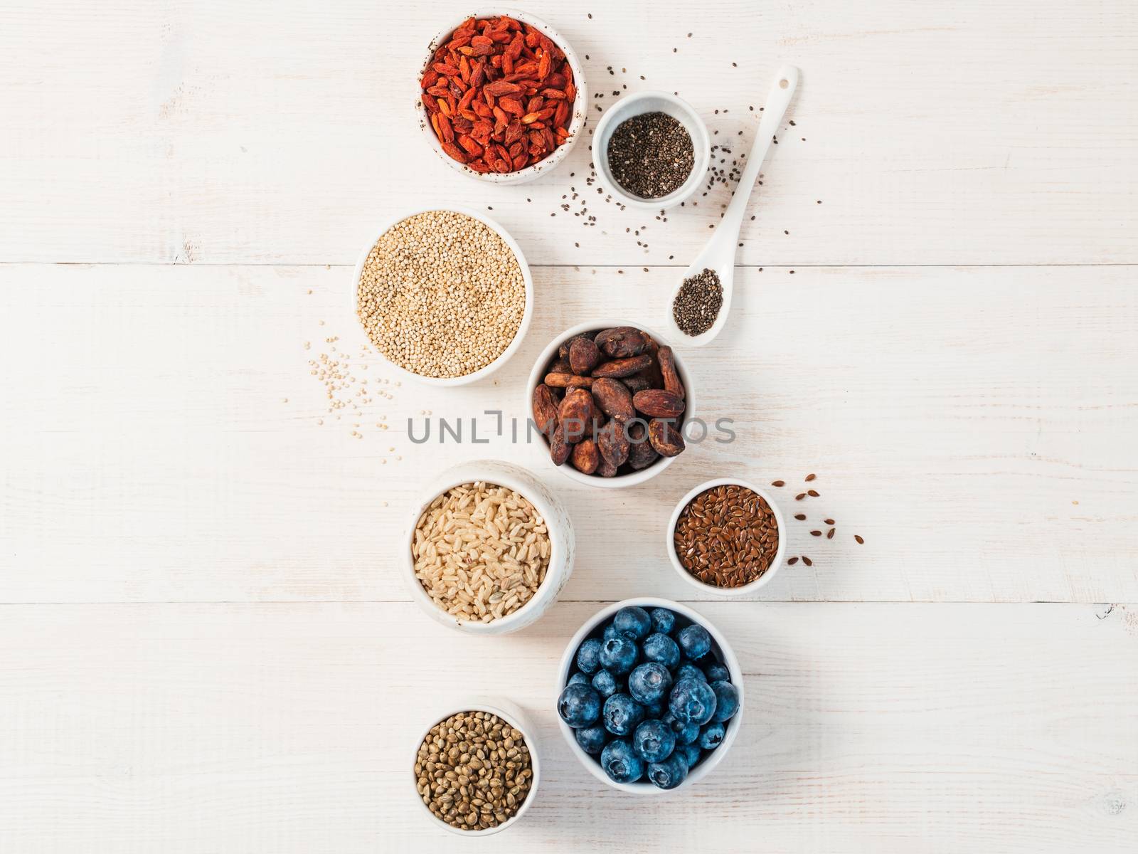 Various superfoods in small bowl on white wooden table.Selection super food.Superfood as blueberry, chia, raw cocoa bean, goji, hemp seeds, quinoa, brown rice. Copy space for text.Top view or flat lay