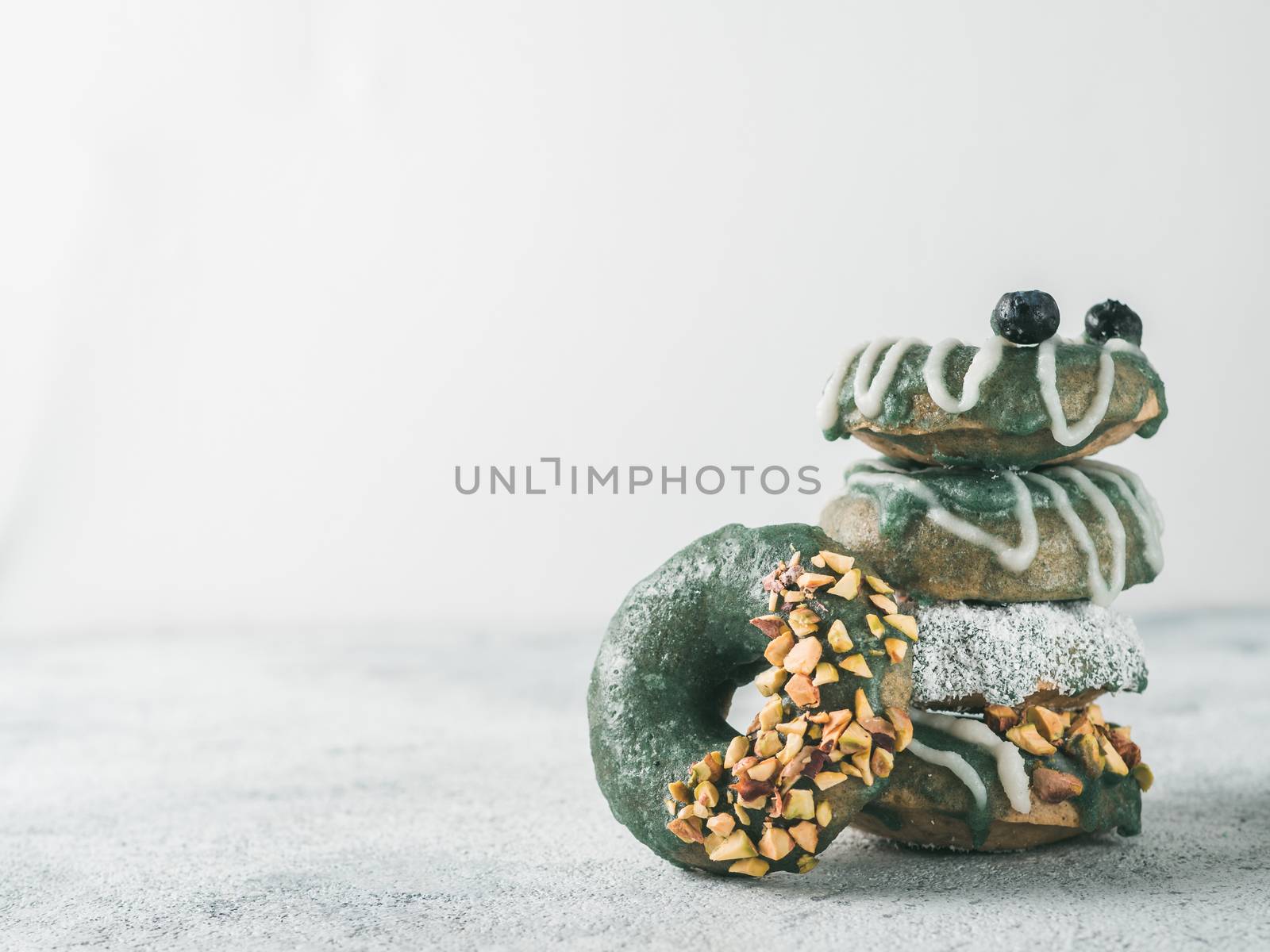 Vegan doughnuts with chia seeds topped with healthy spirulina glaze with pistachio, desiccated coconut and blueberry. Stack of blue green spirulina donuts on gray background. Copy space.