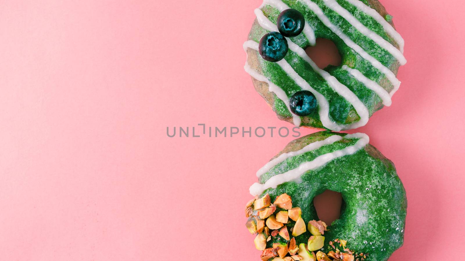 Vegan doughnuts with chia seeds topped with healthy matcha tea glaze with pistachio and blueberry. Green matcha tea donuts on pink background. Copy space. Top view. Banner