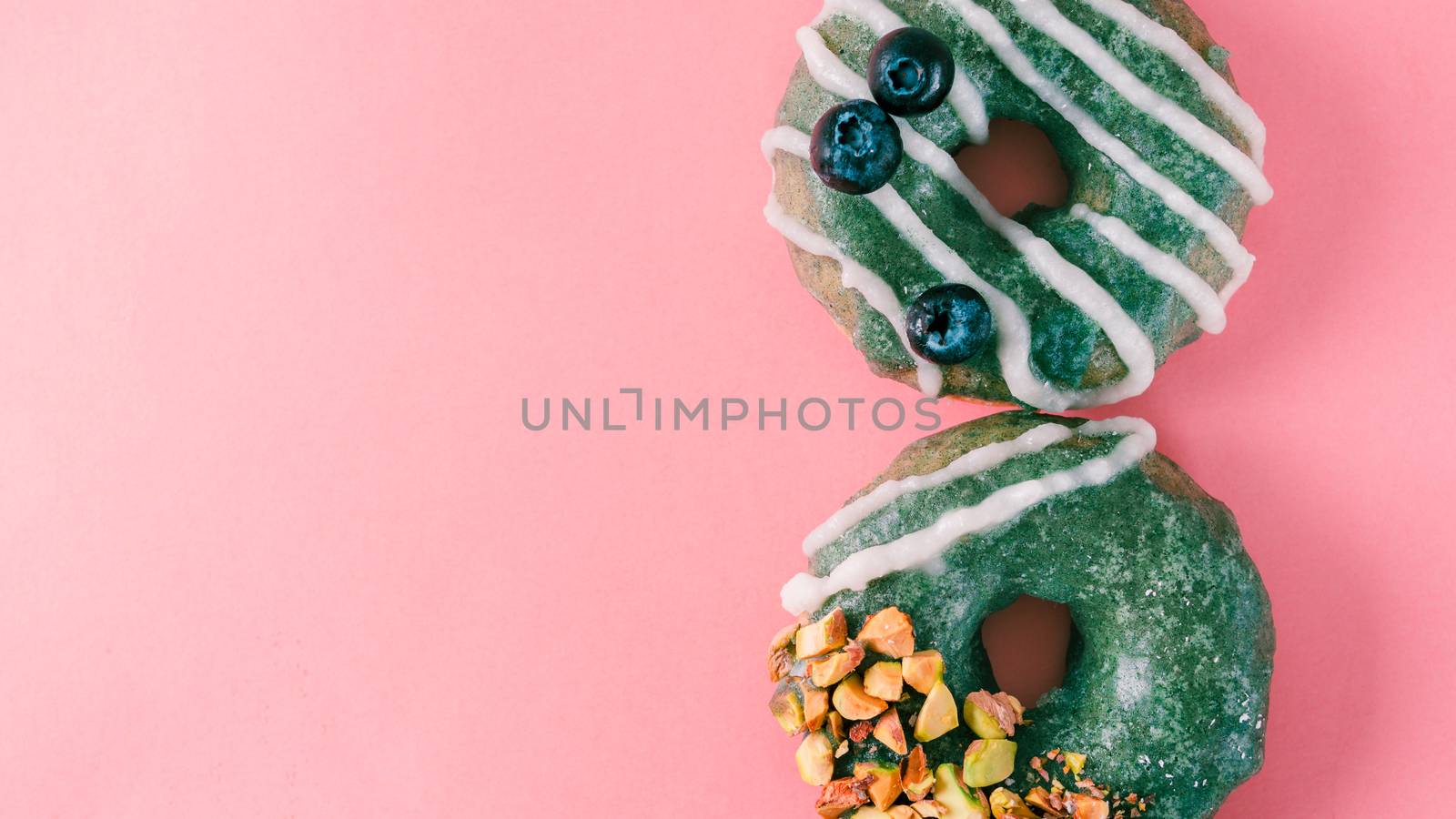 Vegan doughnuts with chia seeds topped with healthy spirulina glaze with pistachio and blueberry. Blue green spirulina donuts on pink background. Copy space. Top view. Banner