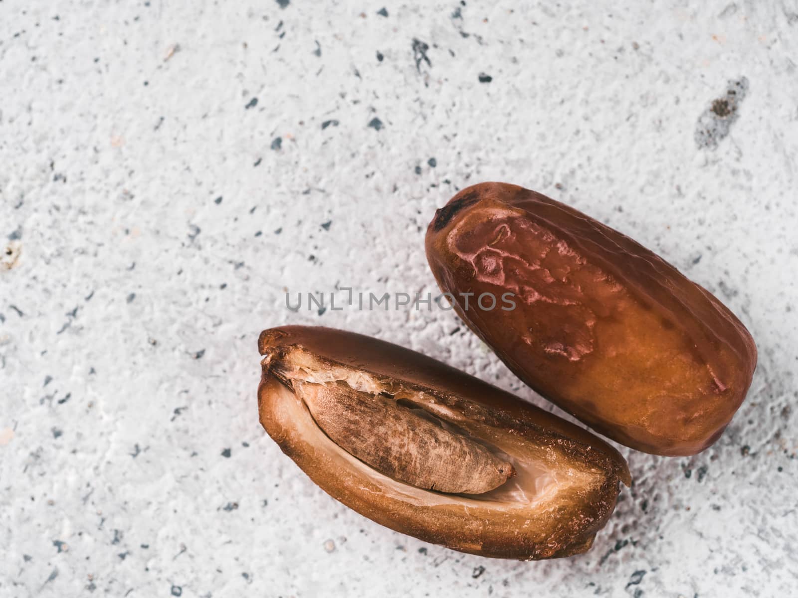Sweet raw dates on gray cement background. Whole dates and half with bone date on grey concrete surface. Sugar free alternatives concept with space for text. Top view. Extreme close up view