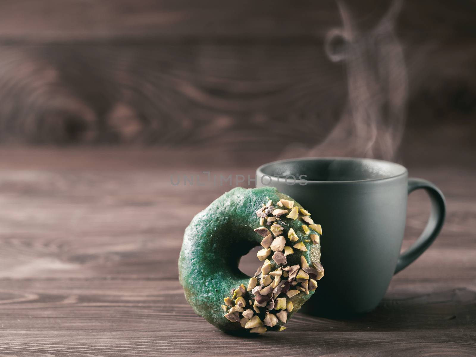 Vegan doughnuts with chia seeds topped with healthy spirulina glaze with pistachio. Blue green spirulina donuts, hot herbal tea cup with steam on brown wooden table. Copy space for text