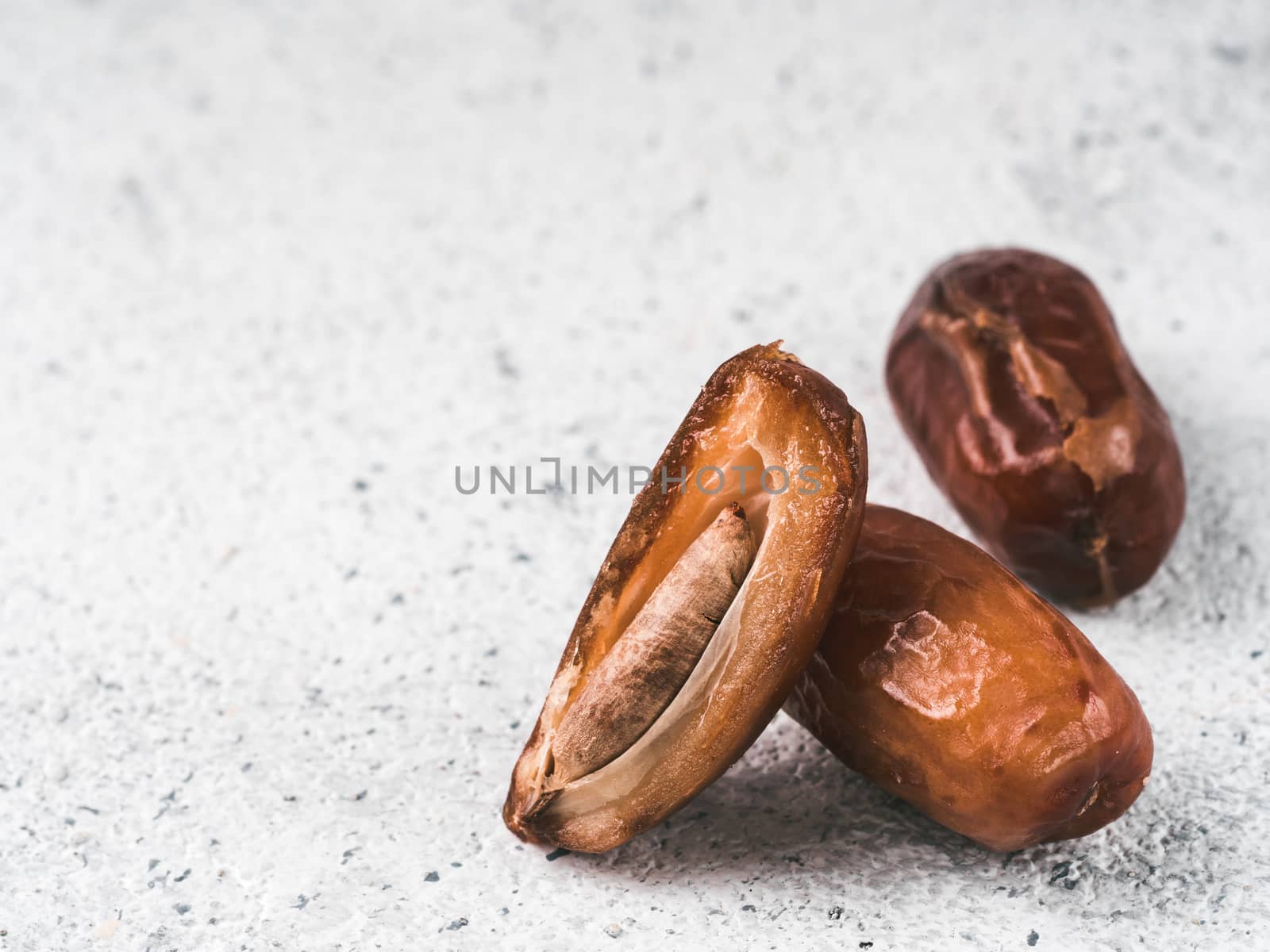 Sweet raw dates on gray cement background. Whole dates and half with bone date on grey concrete surface. Sugar free alternatives concept with space for text. Extreme close up view