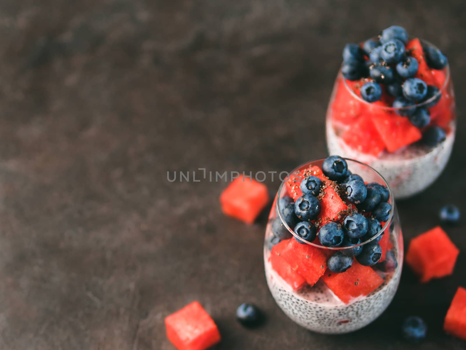 Healthy breakfast concept and idea - chia pudding with watermelon and blueberries. Two glass with chia pudding dressed watermelon and blueberry on dark background. Copy space for text.