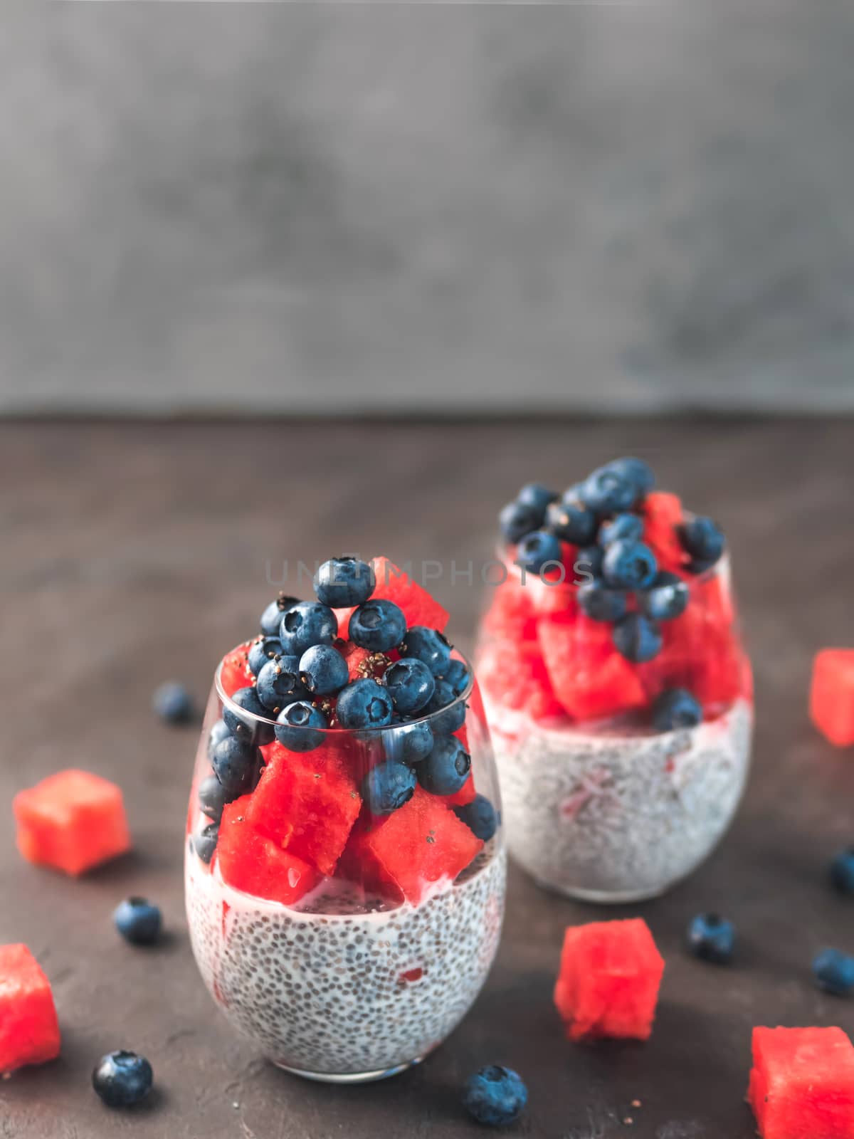 Healthy breakfast concept and idea - chia pudding with watermelon and blueberries. Two glass with chia pudding dressed watermelon and blueberry on dark background. Copy space for text. Vertical.