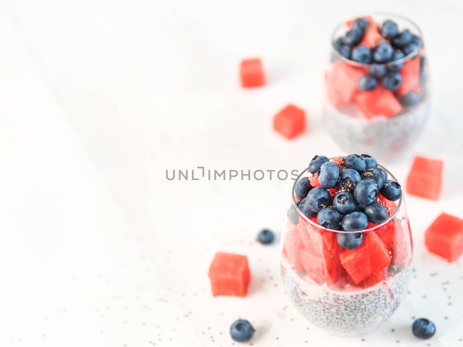 Healthy breakfast concept and idea - chia pudding with watermelon and blueberries. Two glass with chia pudding dressed watermelon and blueberry on white wooden tabletop. Copy space for text.