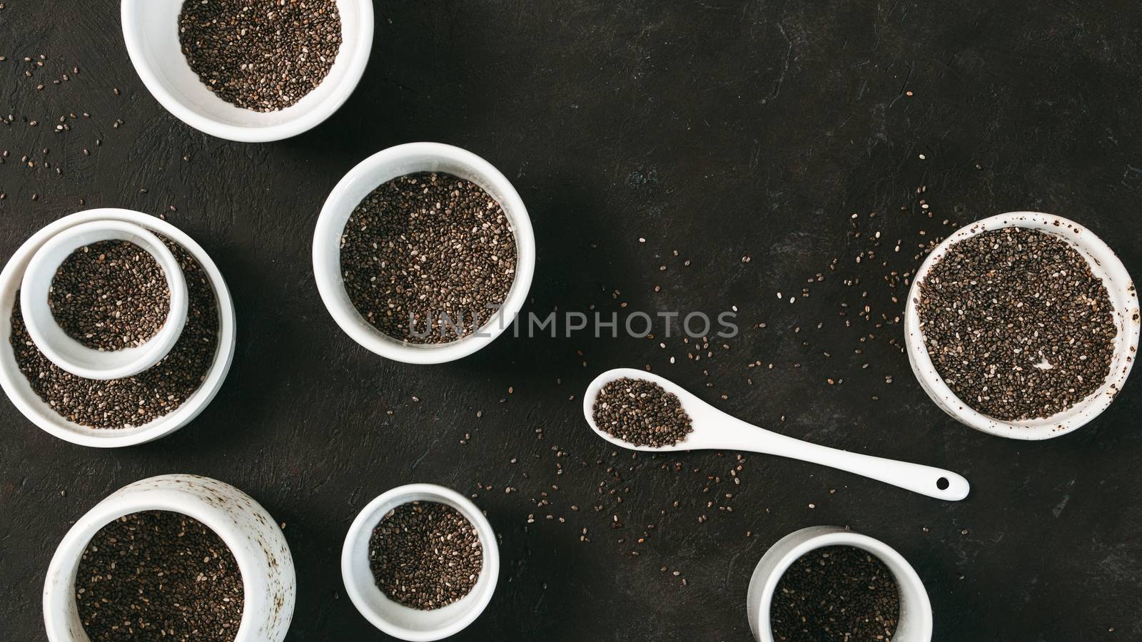 Organic chia seeds on black tabletop. Set of small bowls with organic chia seed. Superfood concept. Copy space. Top view or flat-lay.
