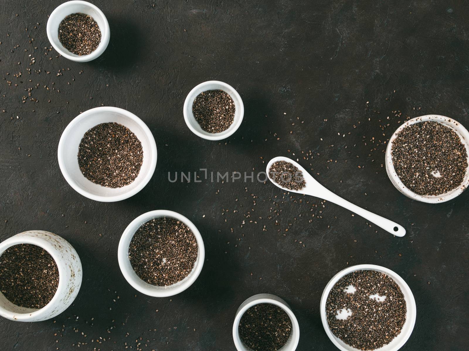 Organic chia seeds on black tabletop. Set of small bowls with organic chia seed. Superfood concept. Copy space. Top view or flat-lay.