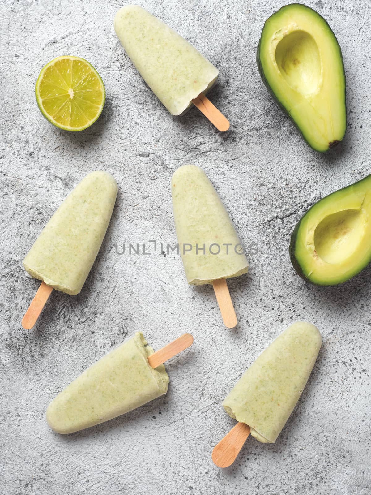 Homemade raw vegan avocado lime popsicle. Sugar-free, non-dairy green ice cream on gray background. Top view. Ideas and recipes for healthy snack, dessert or smoothie. Vertical.