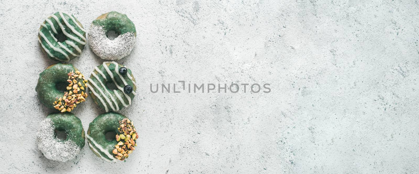 Vegan doughnuts with chia seeds topped with spirulina glaze with pistachio, coconut and blueberry. Blue green spirulina donuts on gray background, top view or flat lay. Copy space for text. Banner