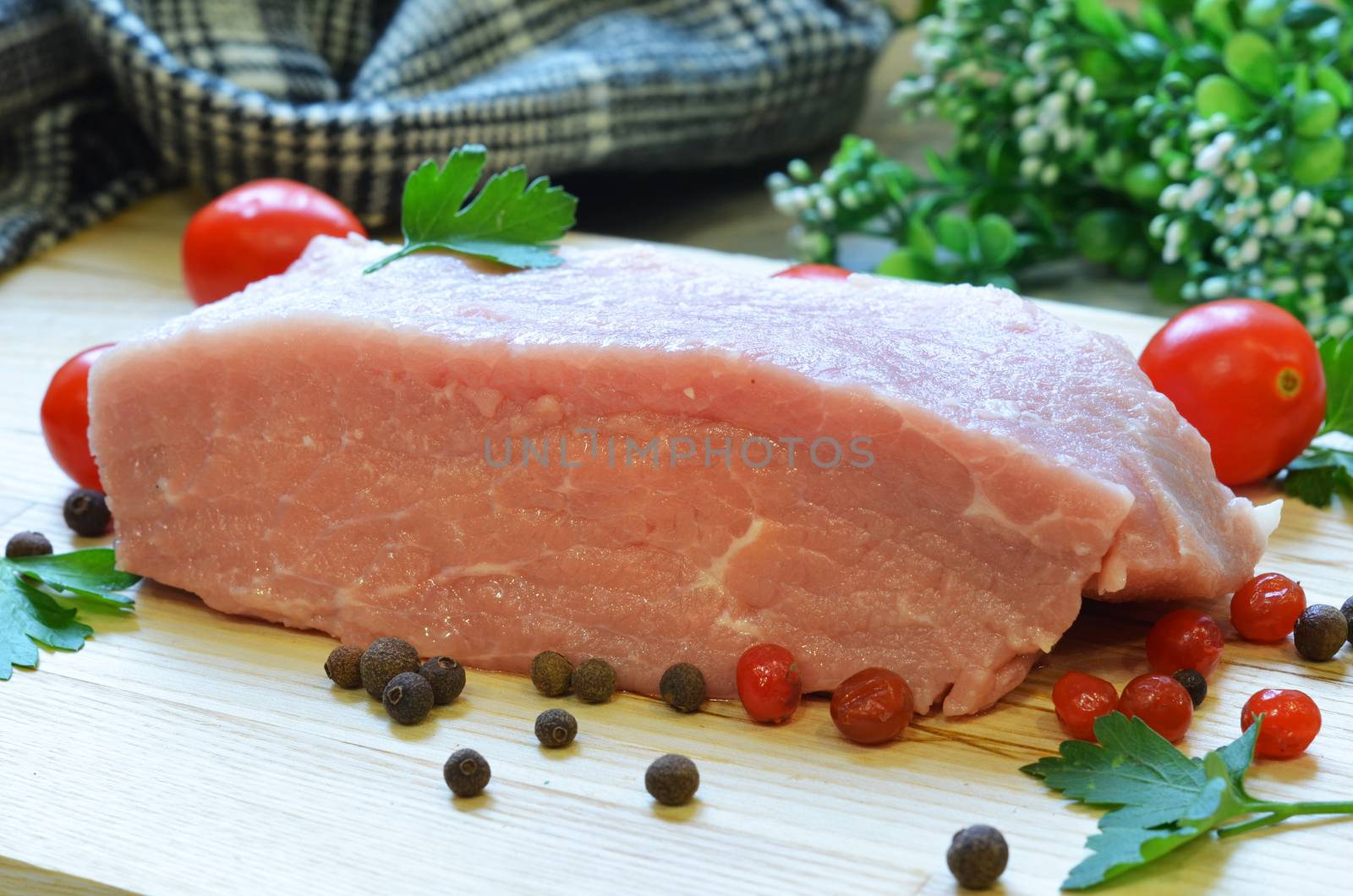 Raw pork meat on cutting board and vegetables and greens.