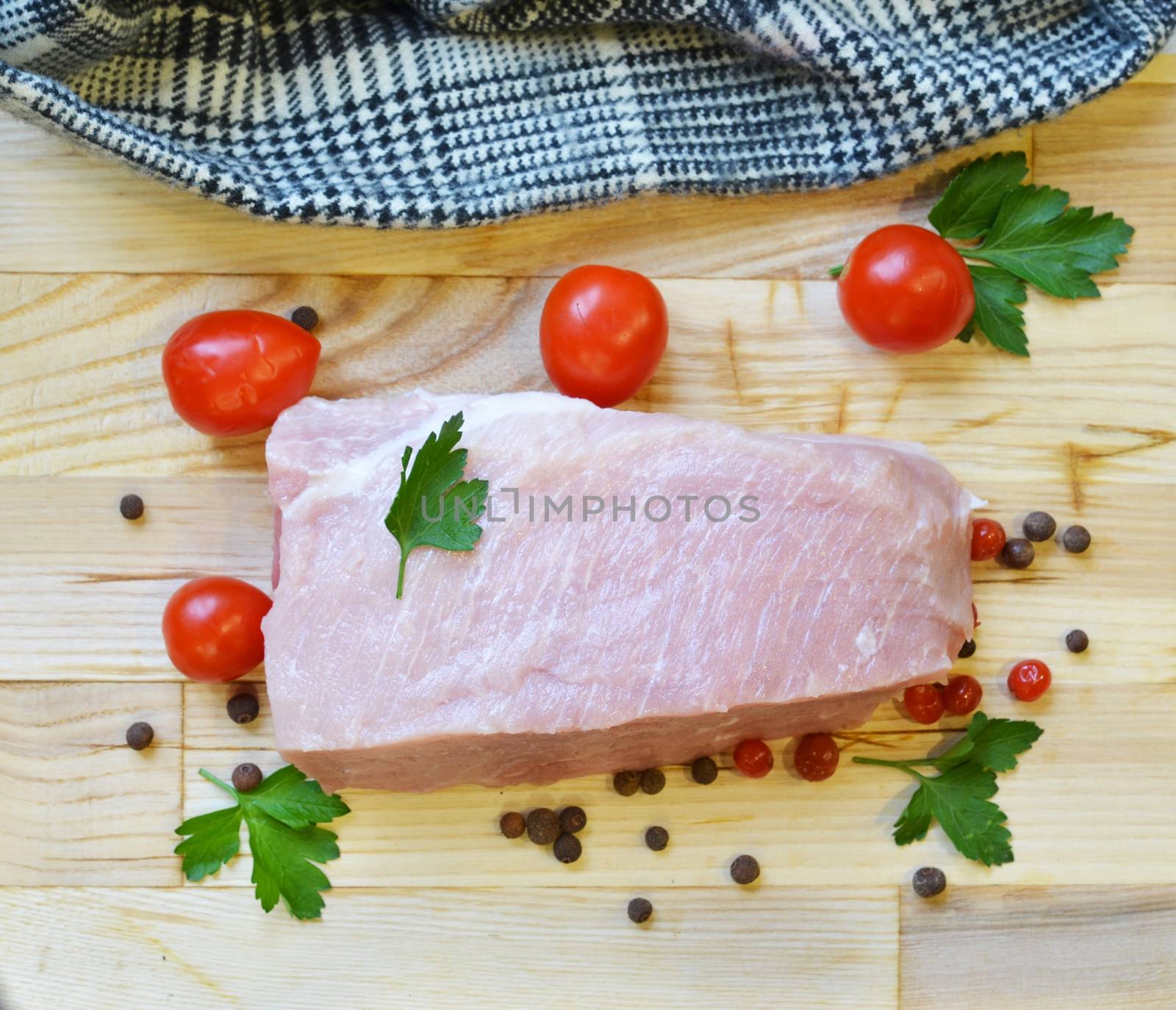 Raw pork meat on cutting board and vegetables and greens.