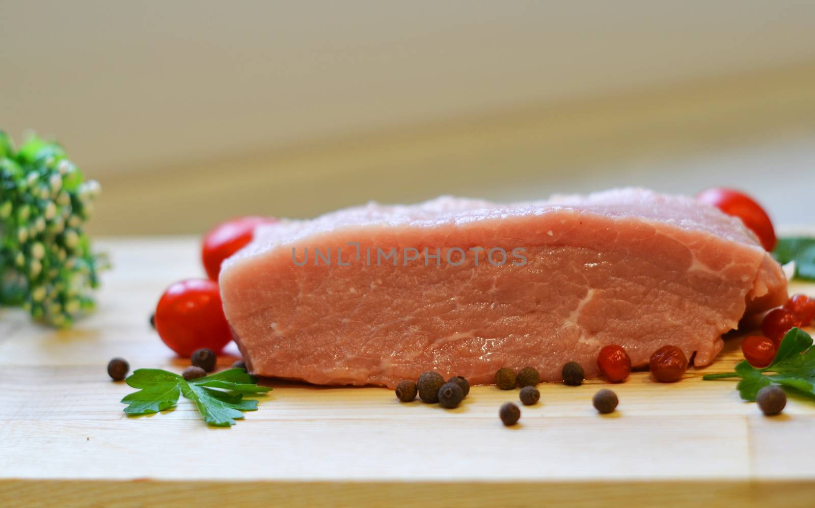 Raw pork meat on cutting board and vegetables and greens.