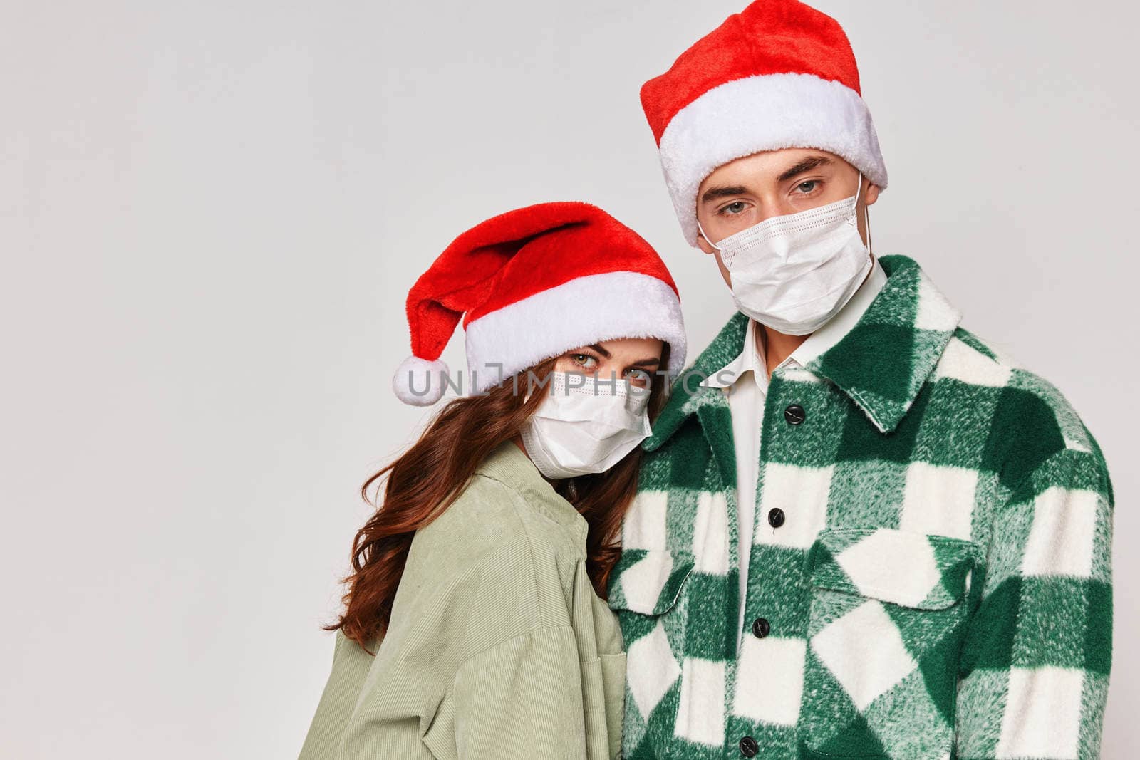 Man and woman in medical masks Christmas hats hugs cropped studio view. High quality photo