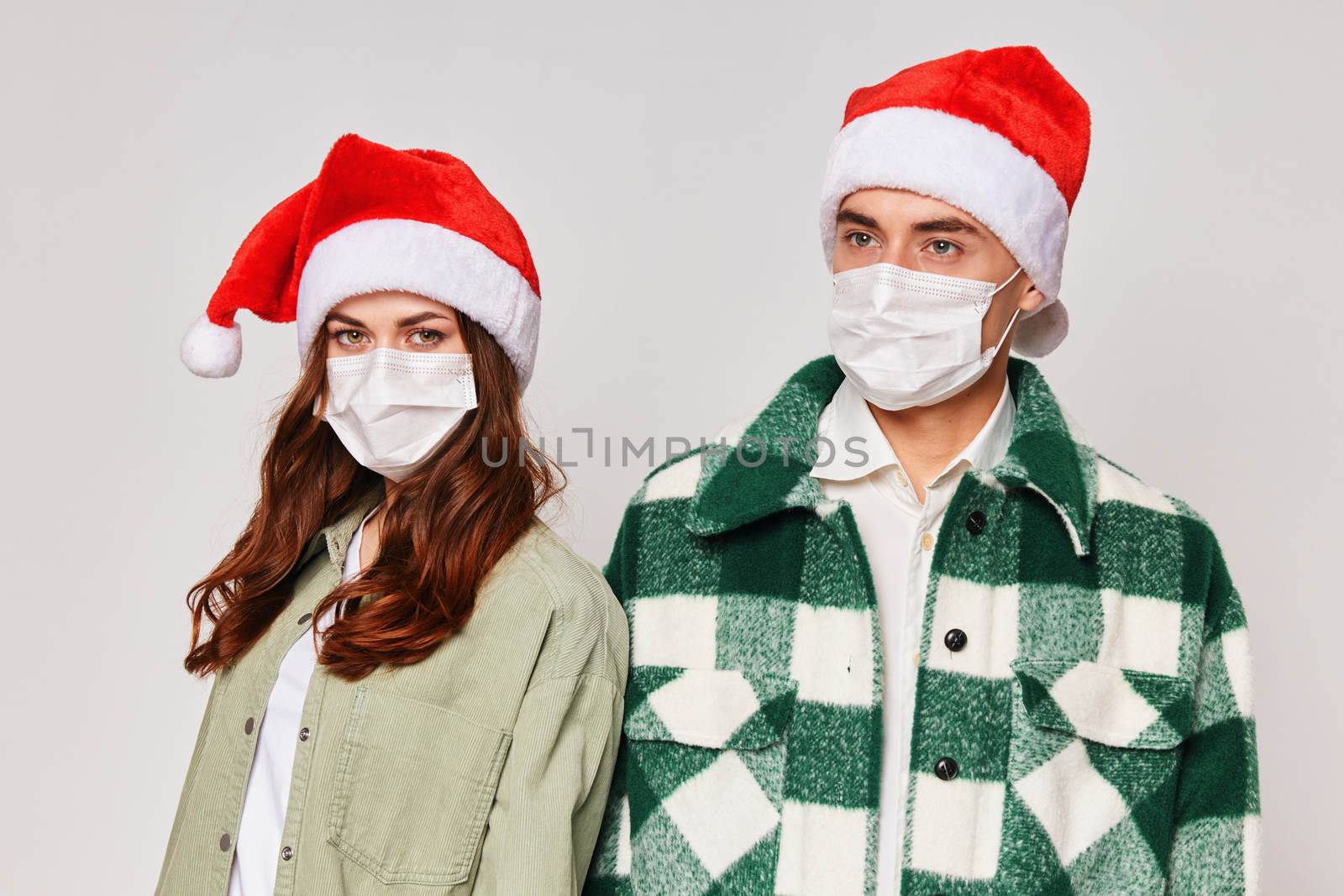 young couple in medical masks on their face christmas hats are standing next to holiday christmas by SHOTPRIME