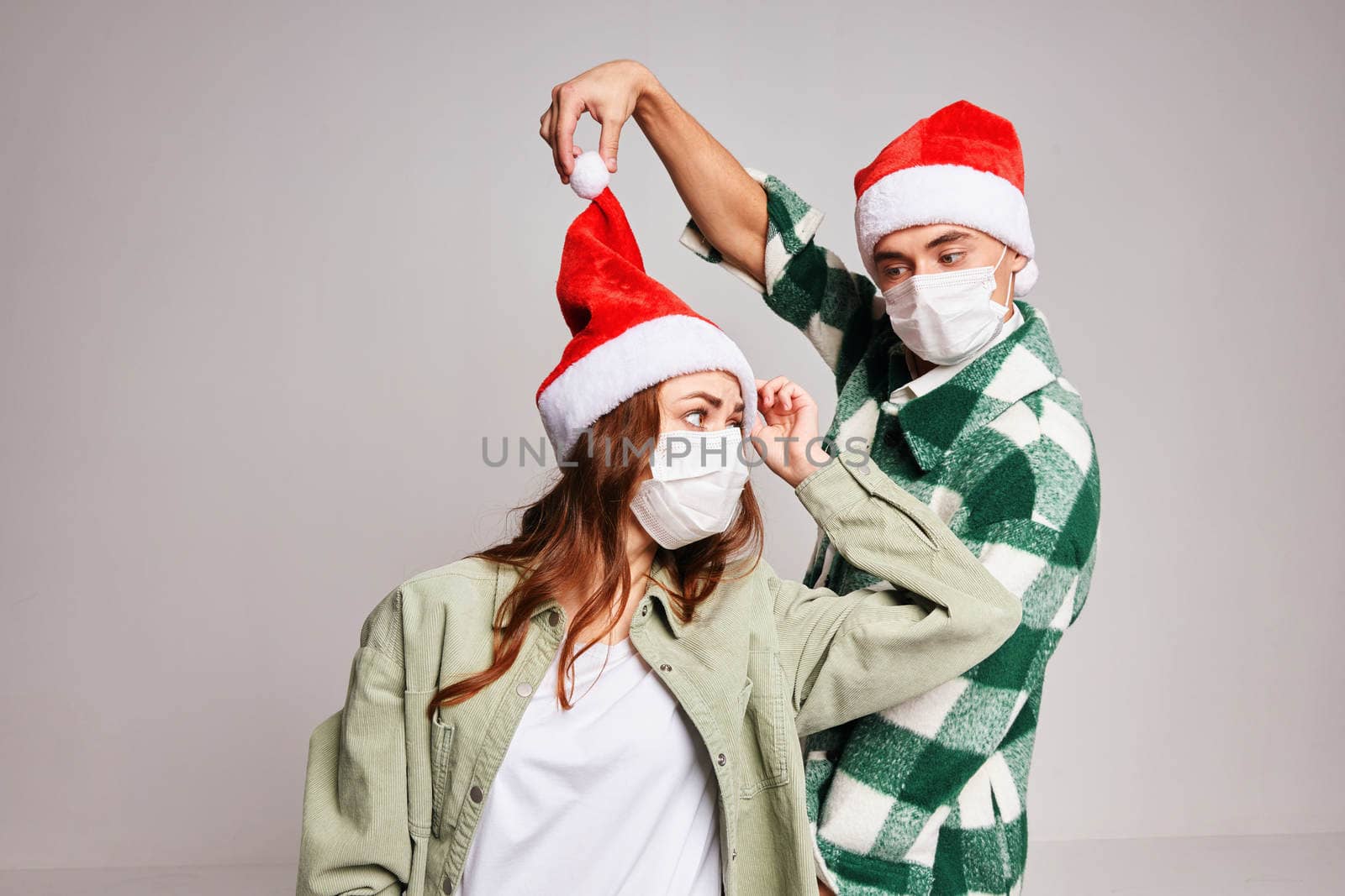 man and woman wearing santa hats christmas fun medical masks studio. High quality photo