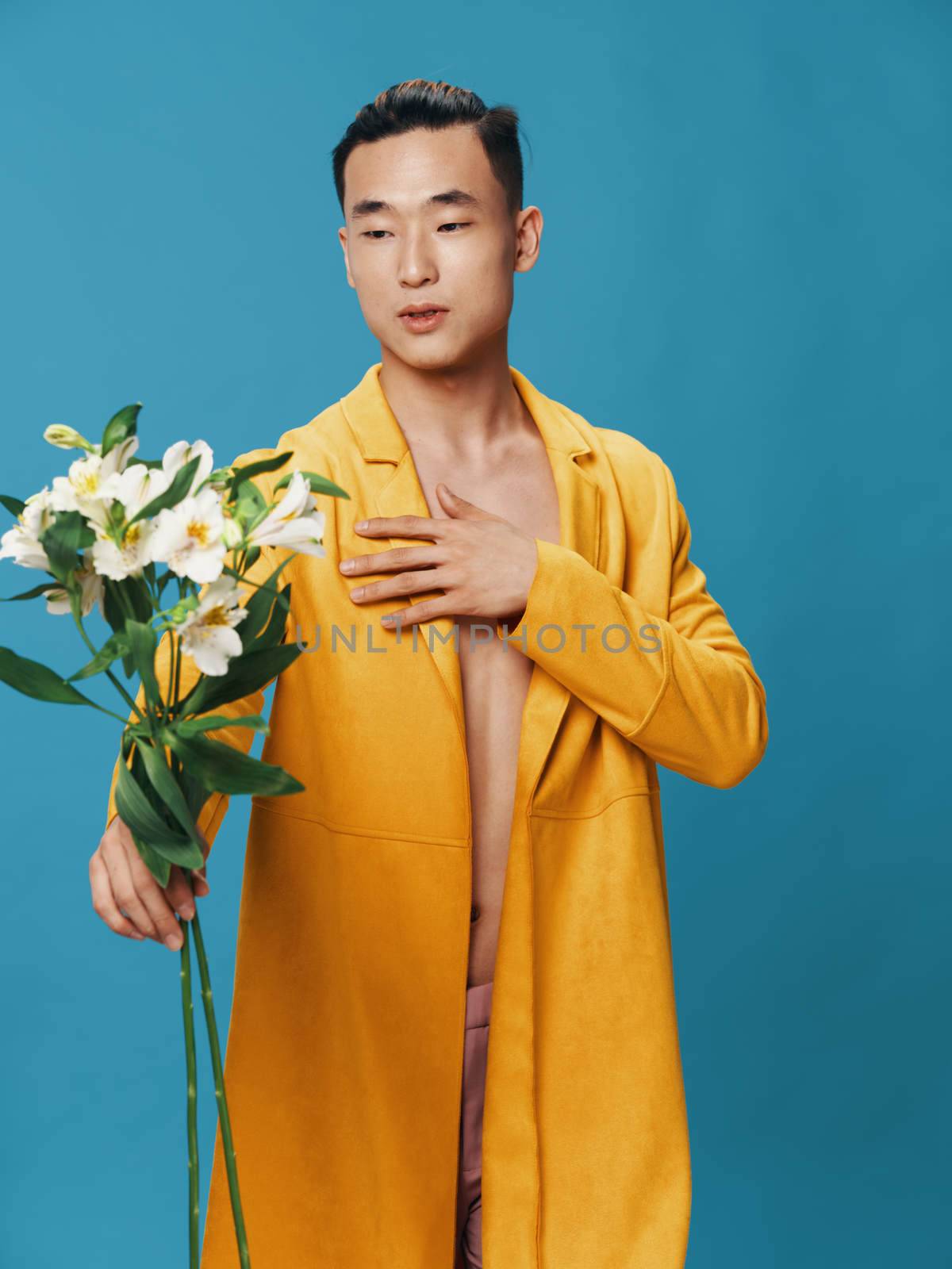 A sexy man in a yellow coat holds a bouquet of white flowers in his hand. High quality photo