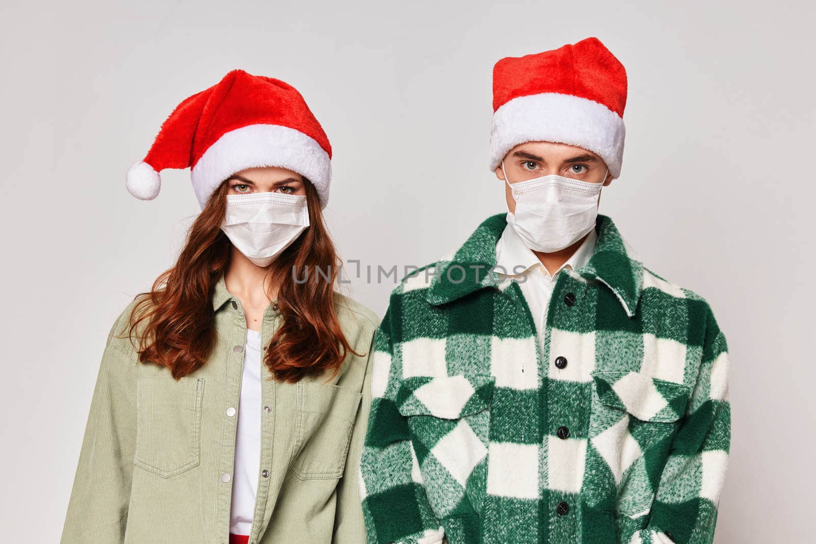 A cute young couple in medical masks are standing next to a Santa hat close-up. High quality photo
