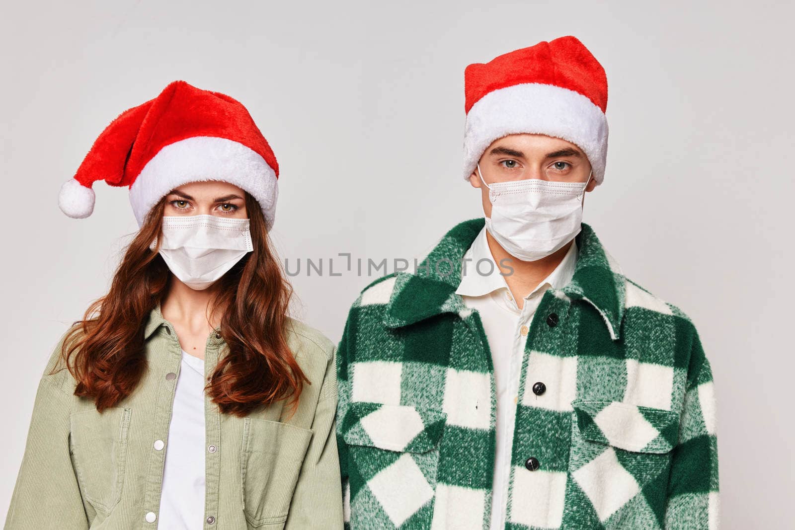 A man and a woman in New Year's Santa hats are standing side by side in medical masks. Close-up protection. Studio by SHOTPRIME