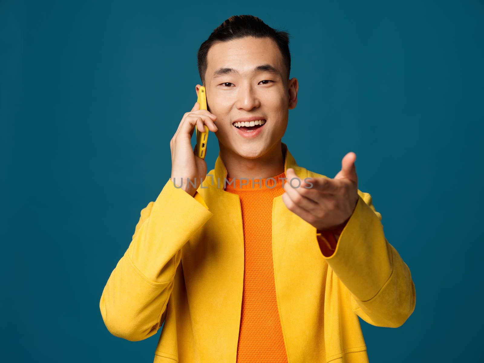 Happy Korean man talking on the phone and gesturing with his hands on a blue background. High quality photo