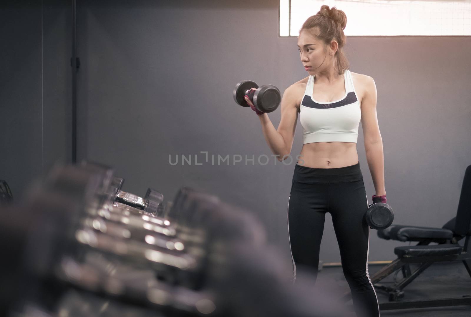 Young healthy woman lifting dumbbells in fitness gym by Surasak