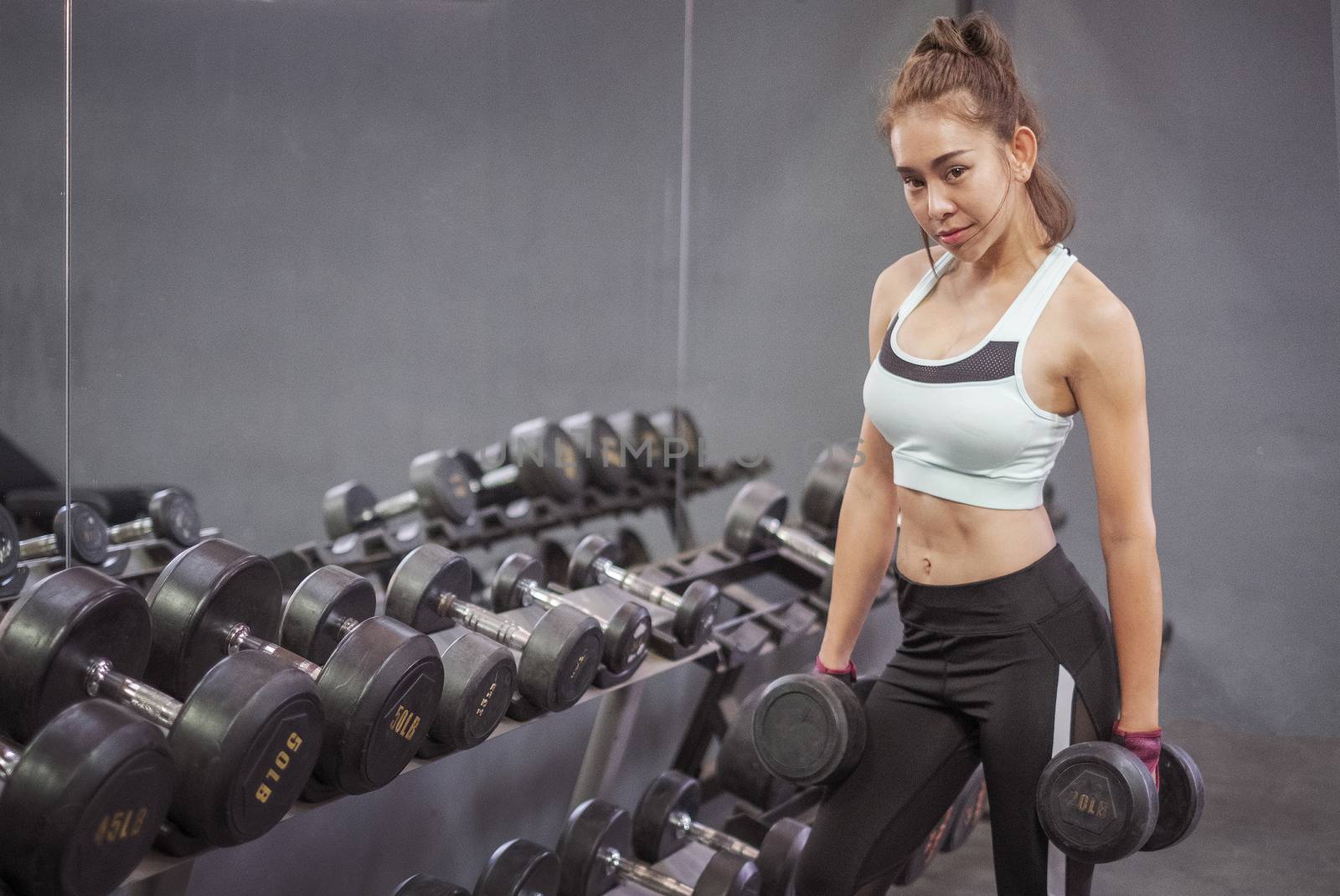 Young healthy woman lifting dumbbells in fitness gym by Surasak