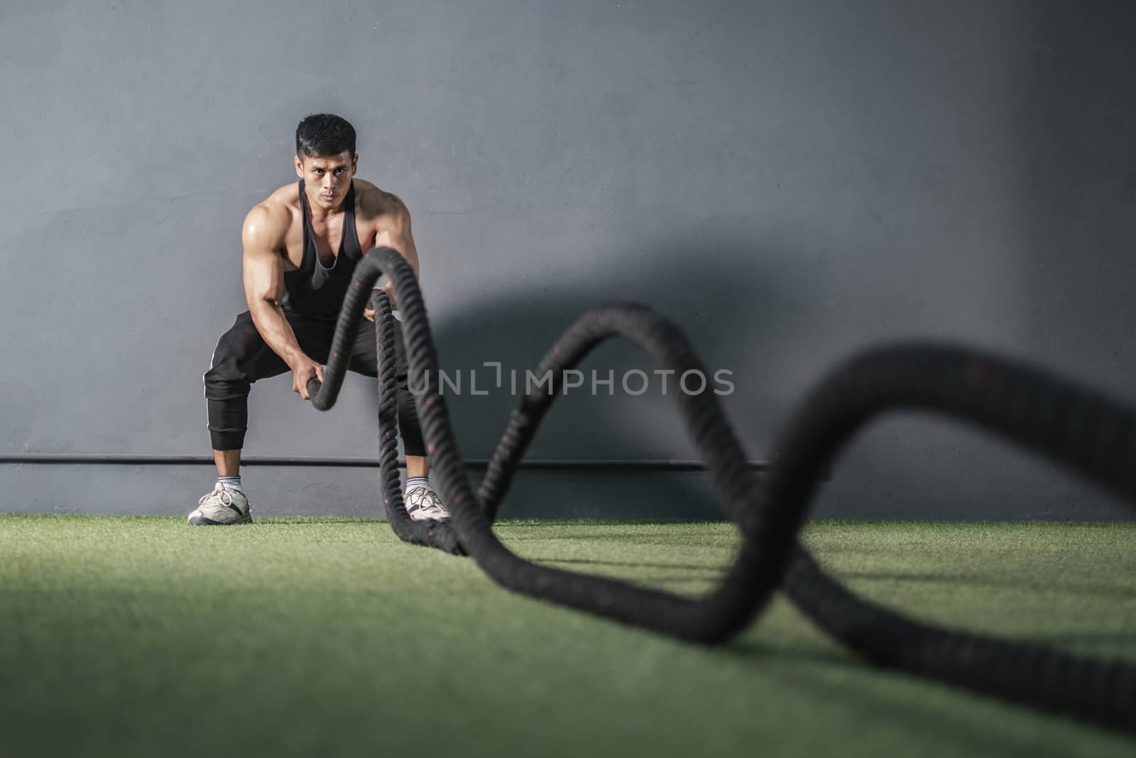 Strong muscle man workout with rope in training fitness gym by Surasak